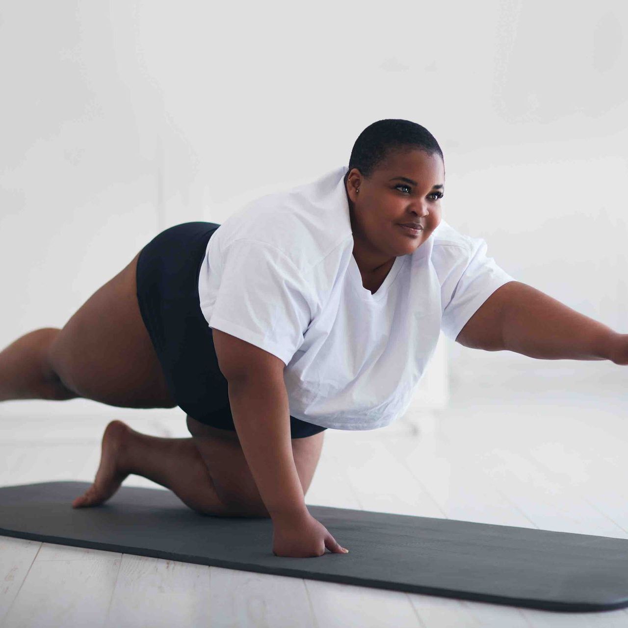 A woman is kneeling on a yoga mat with her arms outstretched