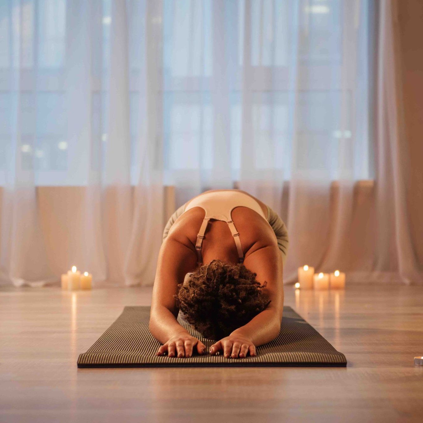 A woman is bending over on a yoga mat in a room with candles.