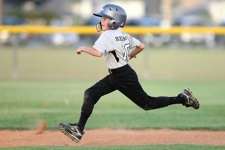 Young baseball player in helmet running hard on a dirt basepath during a game