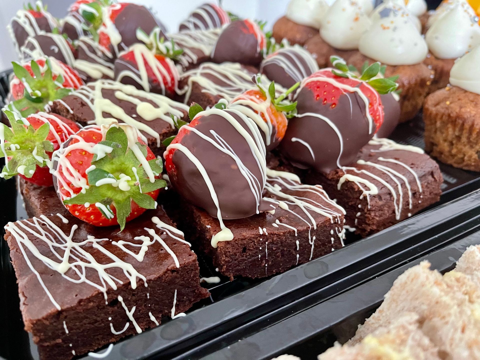 A tray of chocolate covered strawberries and brownies on a table.