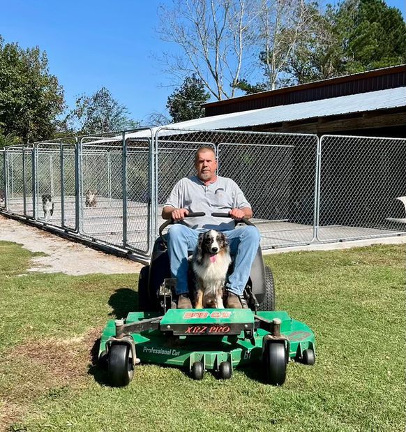 A man is riding a lawn mower with a dog on it.