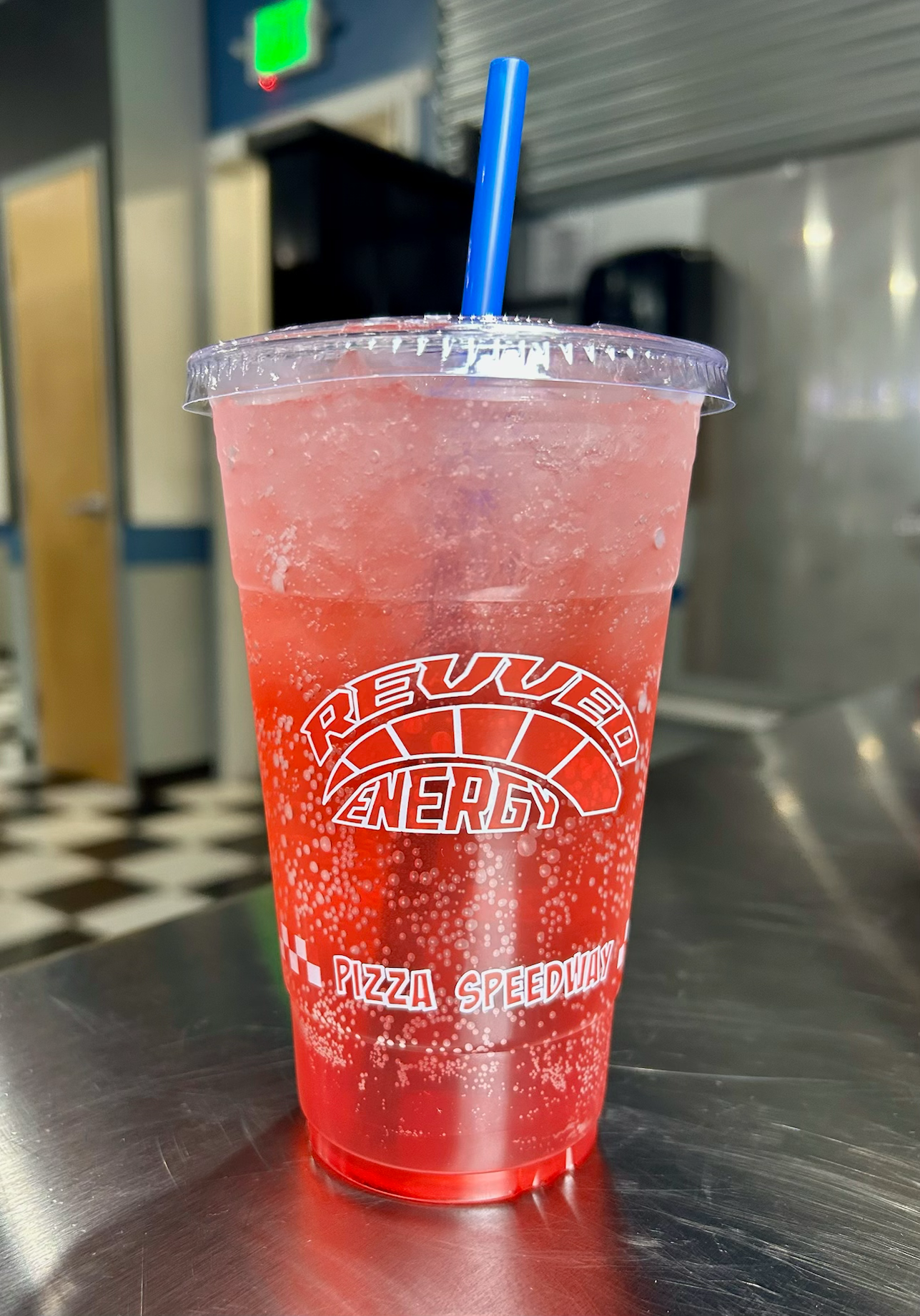 A cup of red liquid with a blue straw on a table.