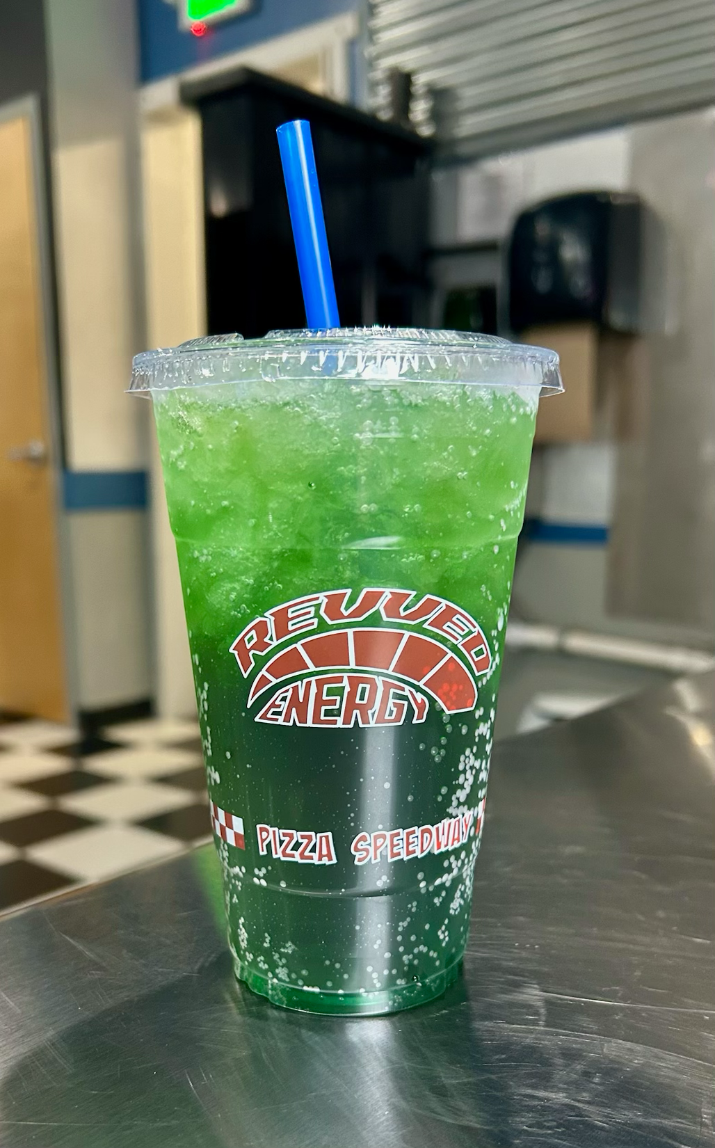 A cup of green soda with a blue straw in it.