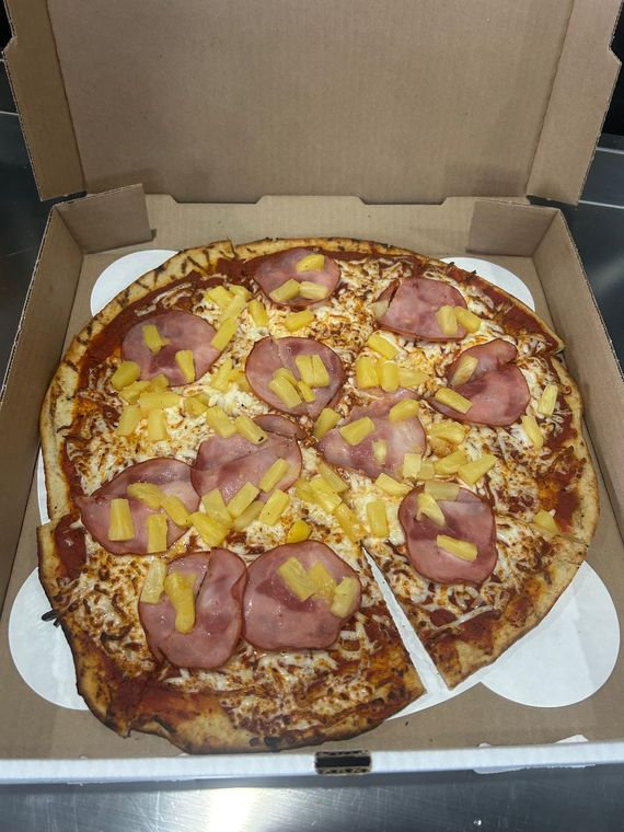 A pizza with ham and pineapple is in a cardboard box.