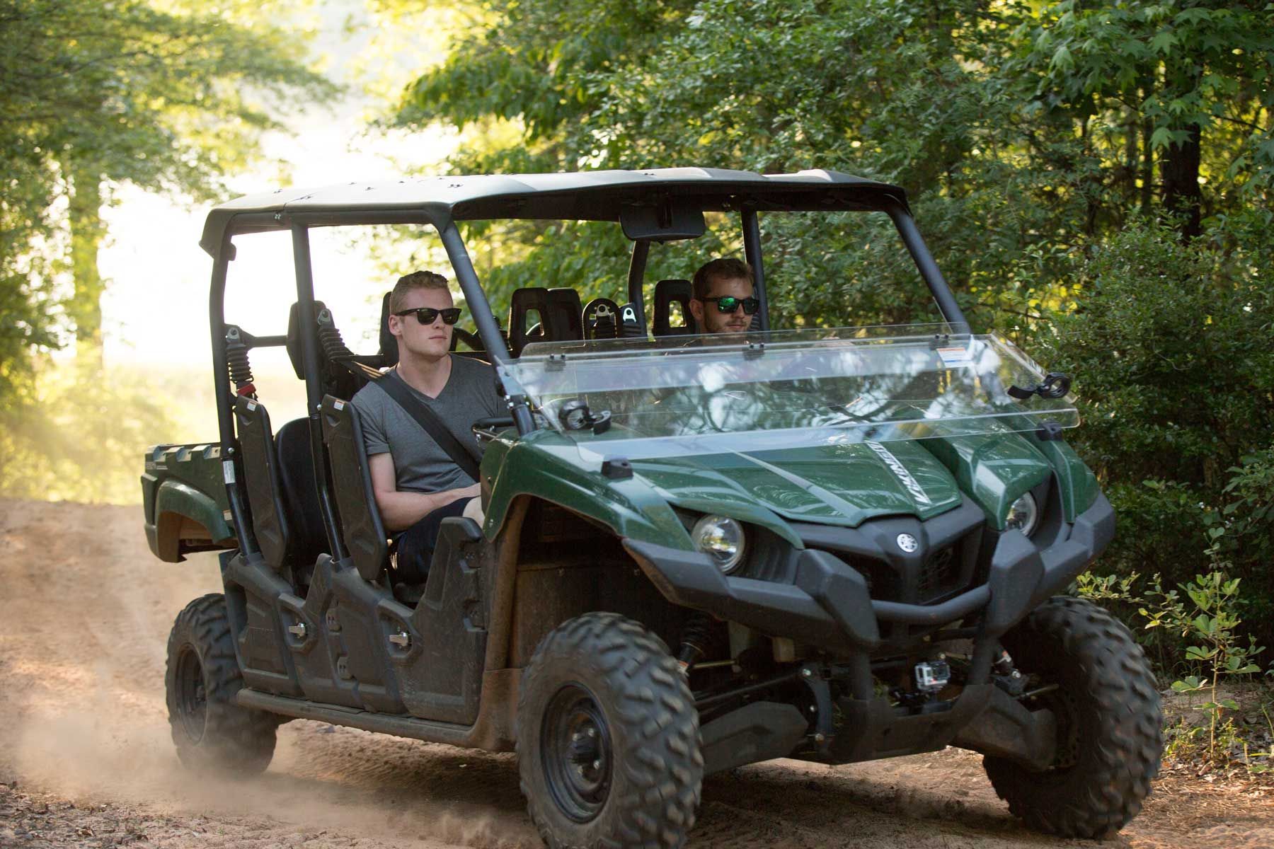 Two men are riding a green atv on a dirt road.