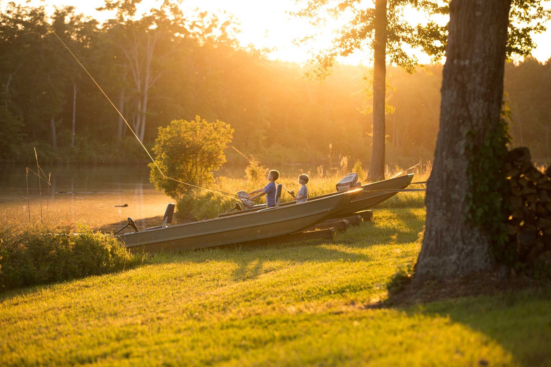 A man is fishing in a boat on a lake at sunset.