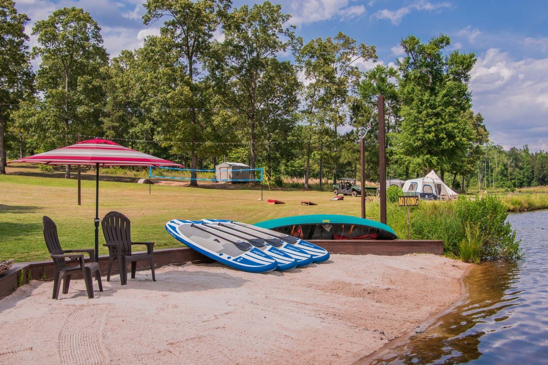 A beach with chairs , umbrellas , kayaks and a volleyball net.