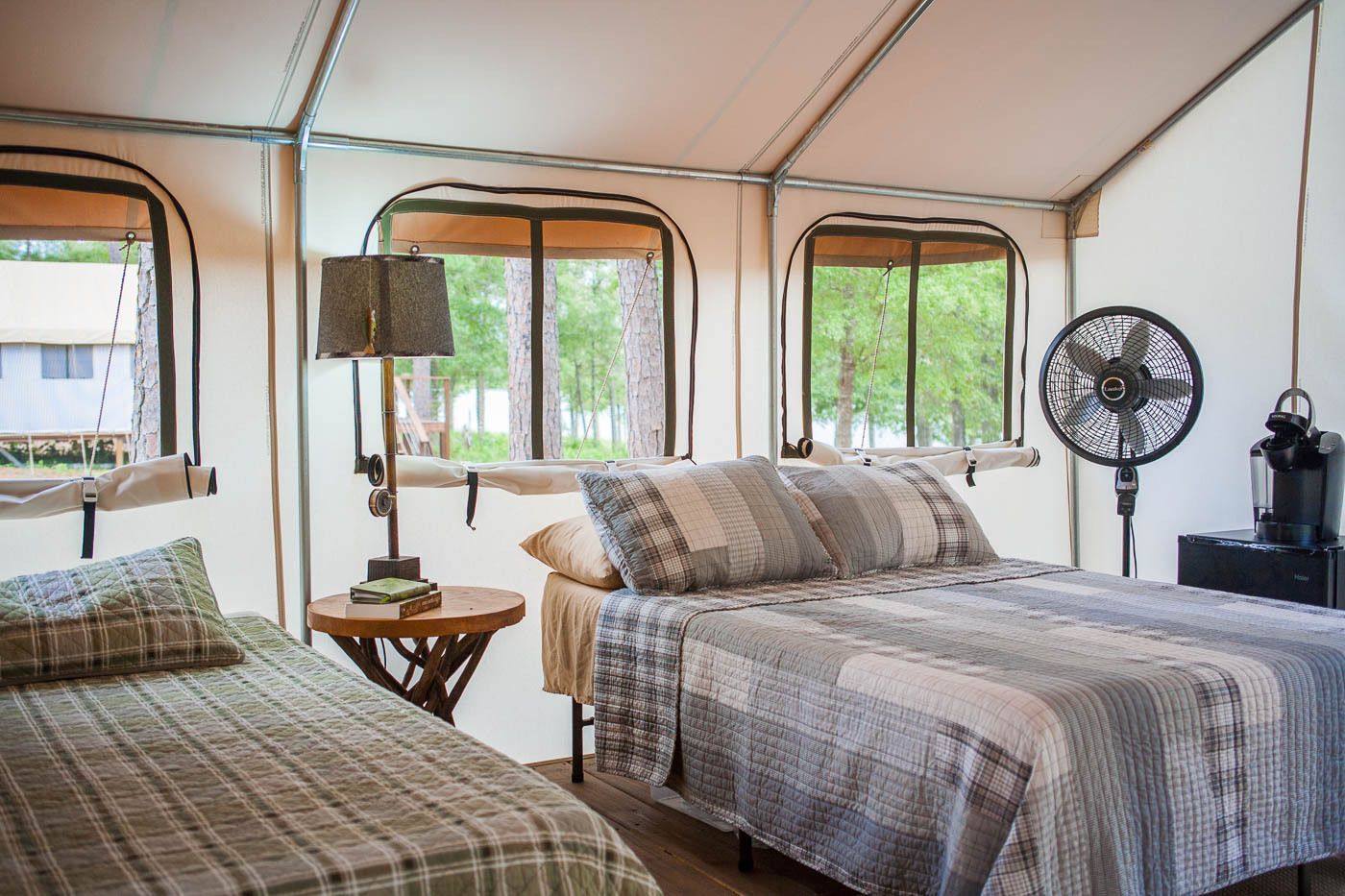 A tent with two beds , a lamp , and a fan.