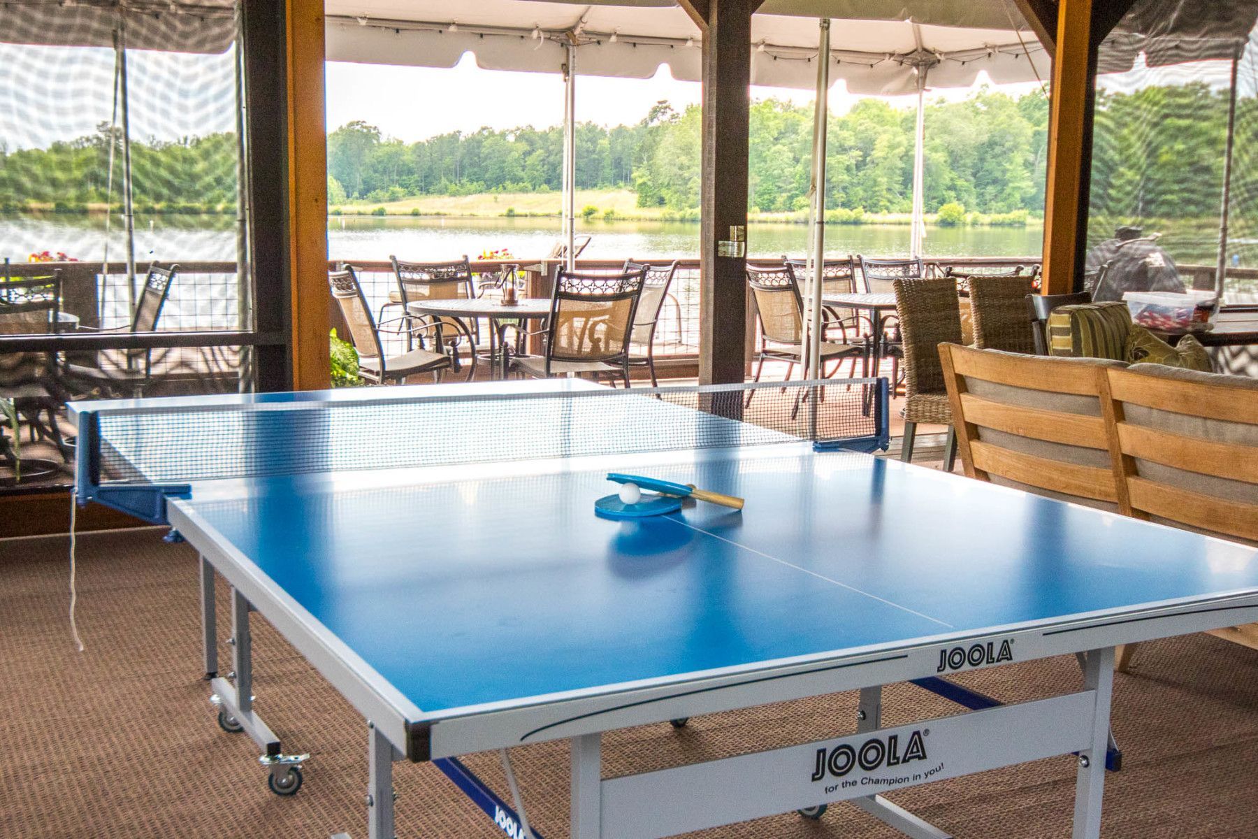 A blue and white ping pong table in a room with a lake in the background.