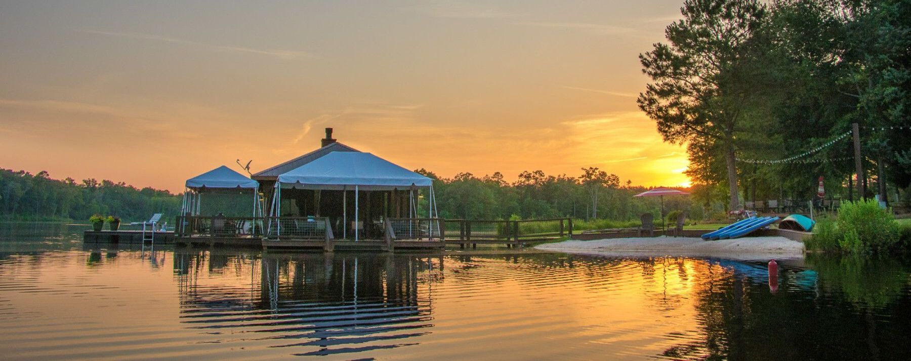 A dock with a gazebo on it in the middle of a lake at sunset.