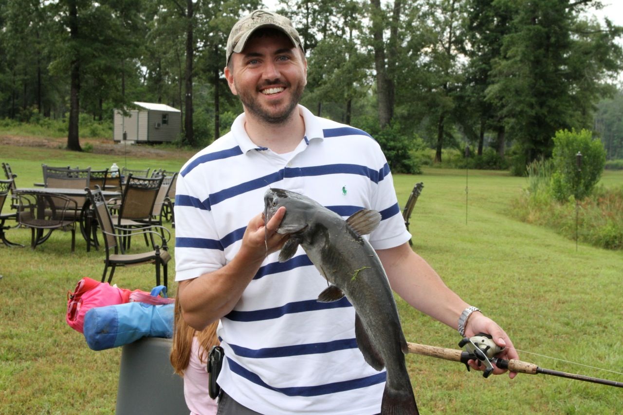 A man in a striped shirt is holding a fish and a fishing rod.