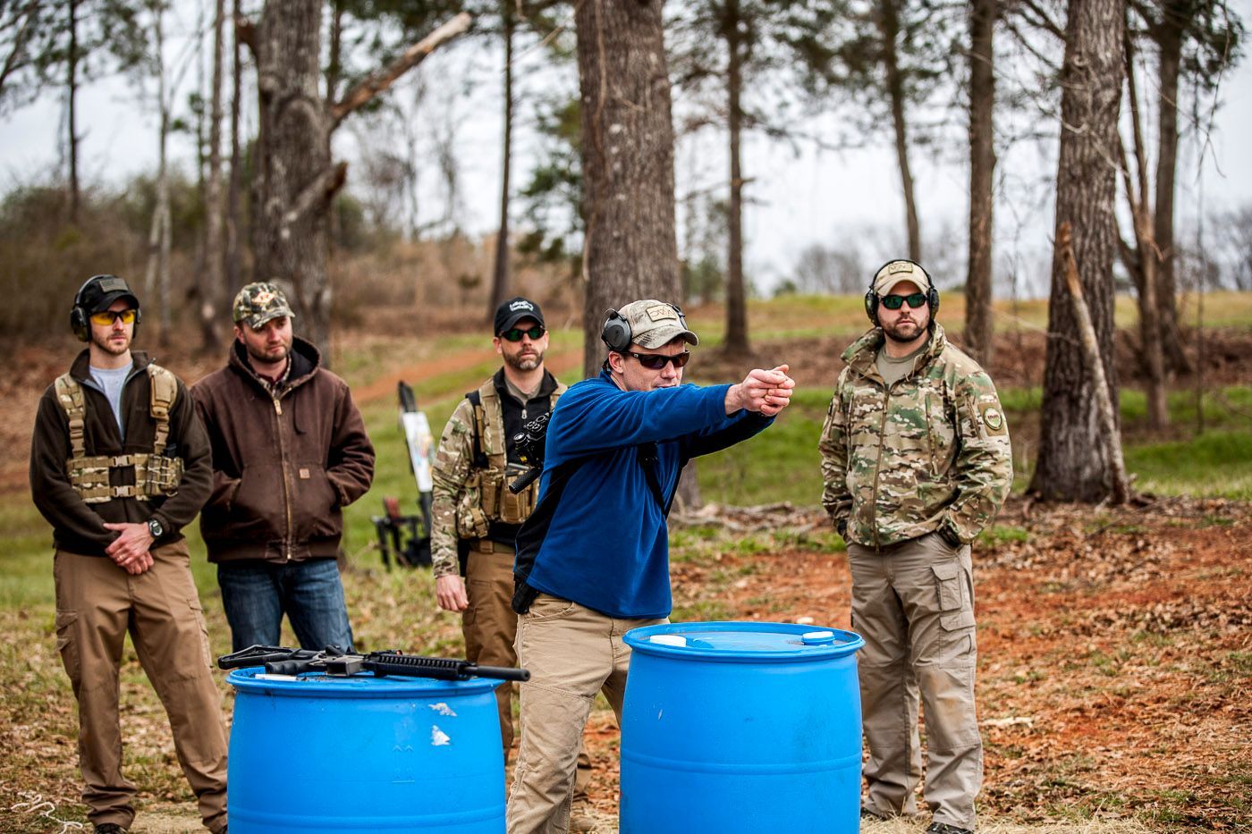 A group of men are standing around two blue barrels.