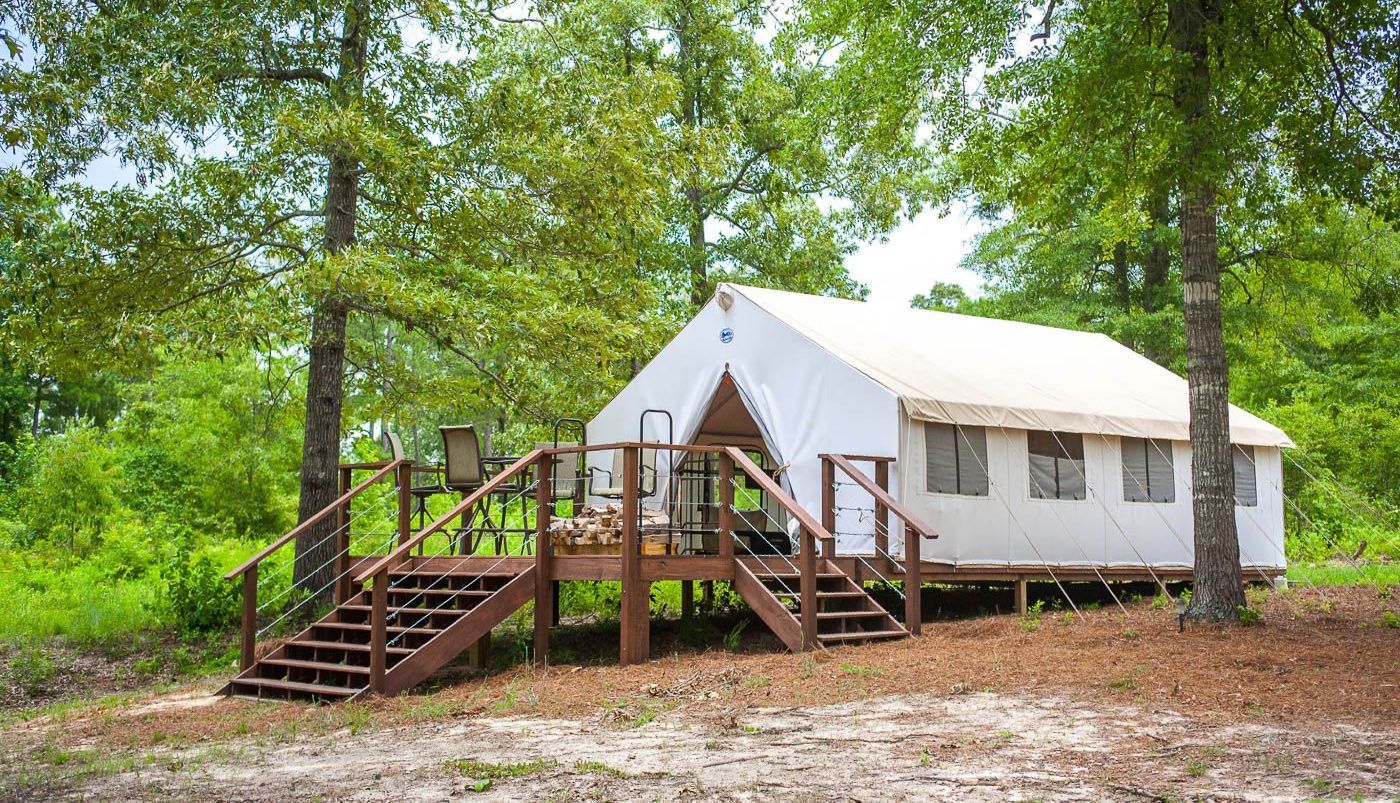 A white tent is sitting on top of a wooden platform in the middle of a forest.