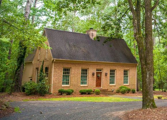 A brick house with a black roof is surrounded by trees.