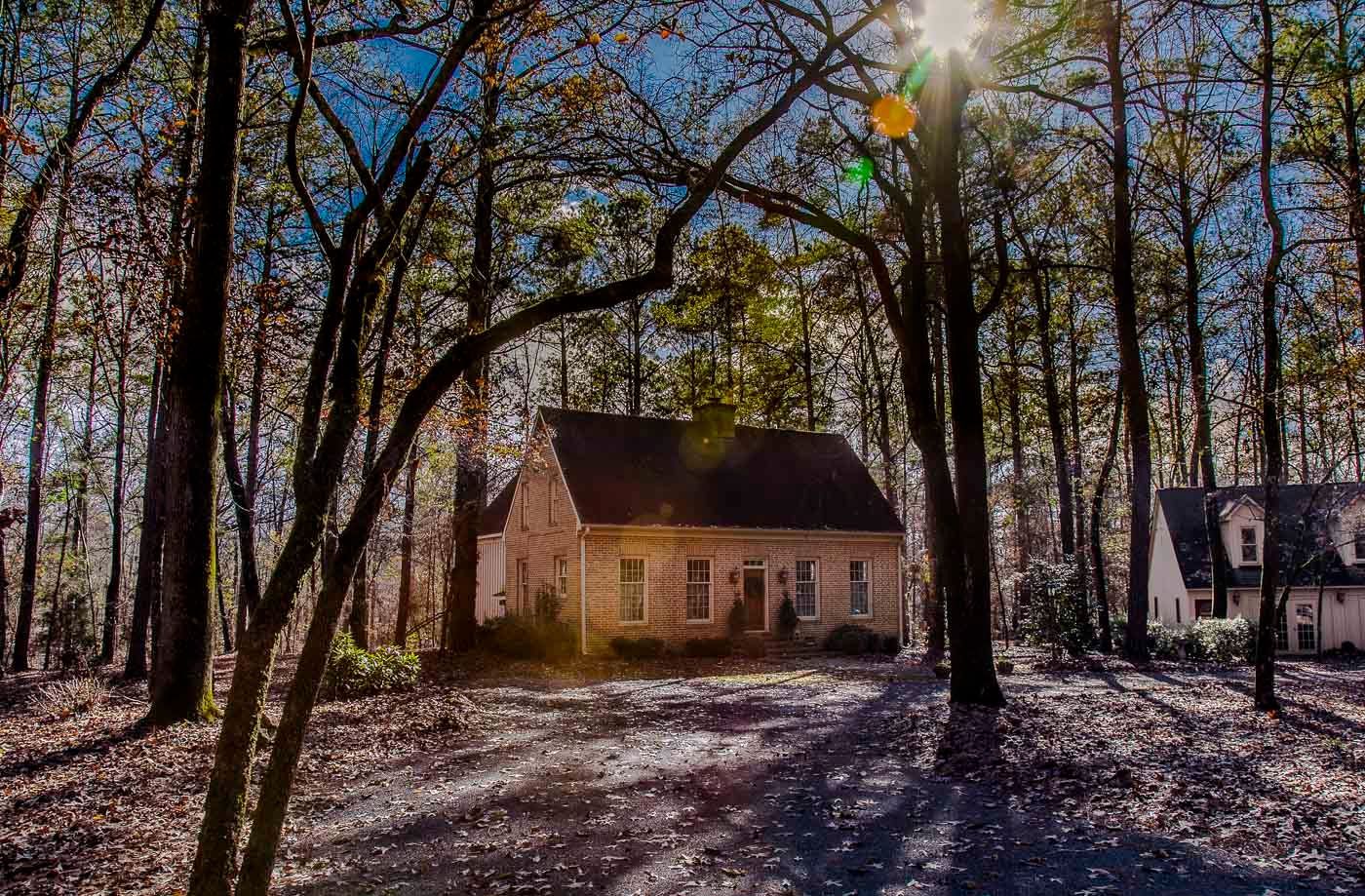 A house in the middle of a forest with the sun shining through the trees.