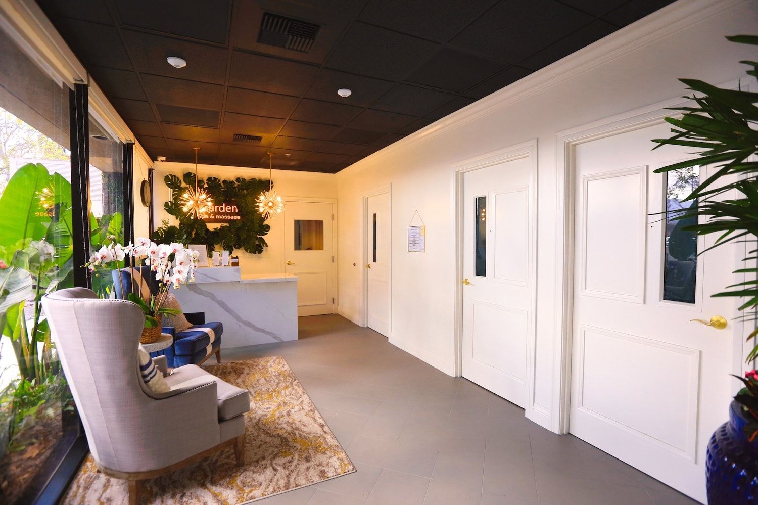 Bright reception area with white doors, gray floor, marble counter, and a window with plants.