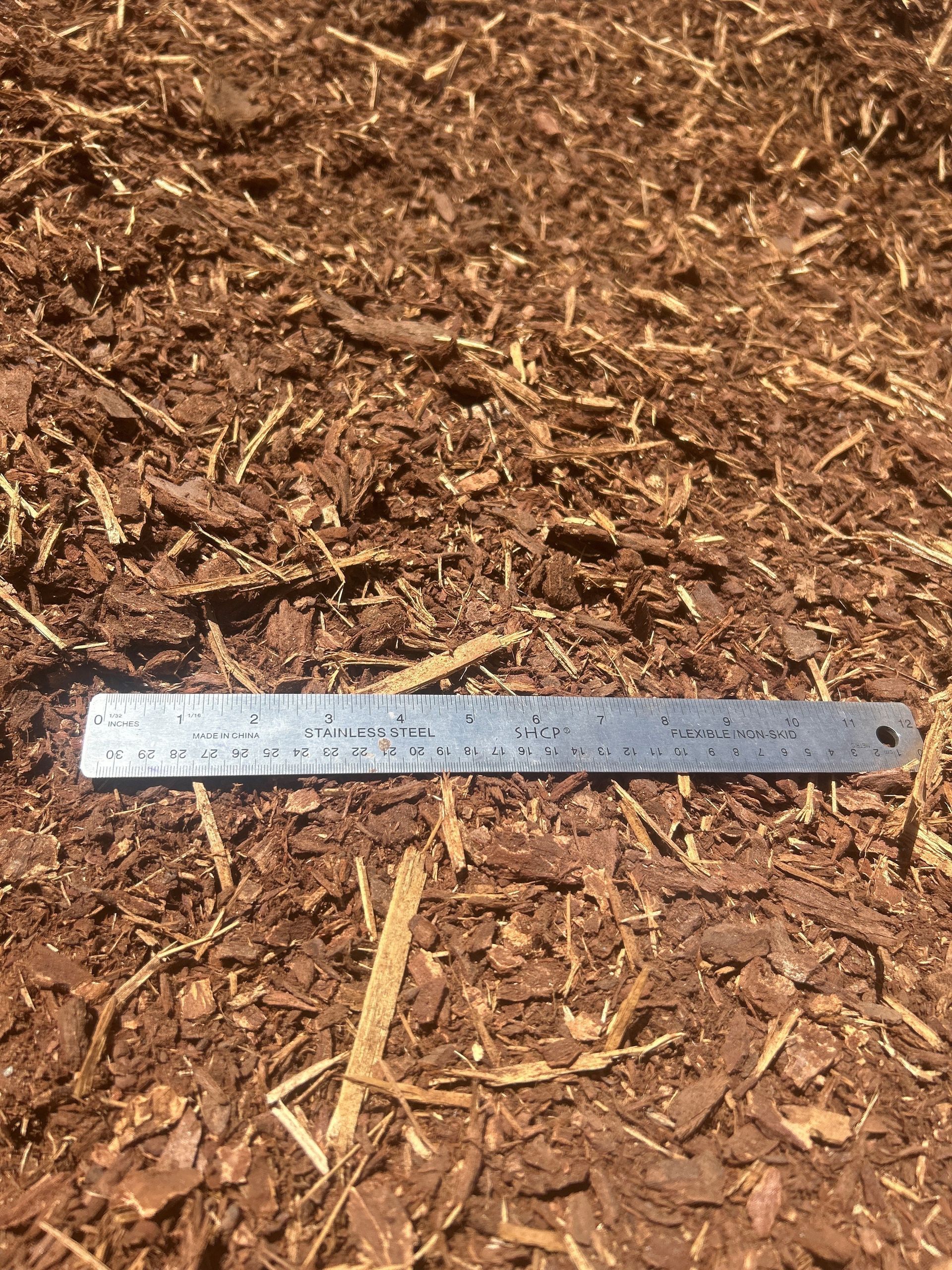 Brown mulch with a metal ruler laid across it.