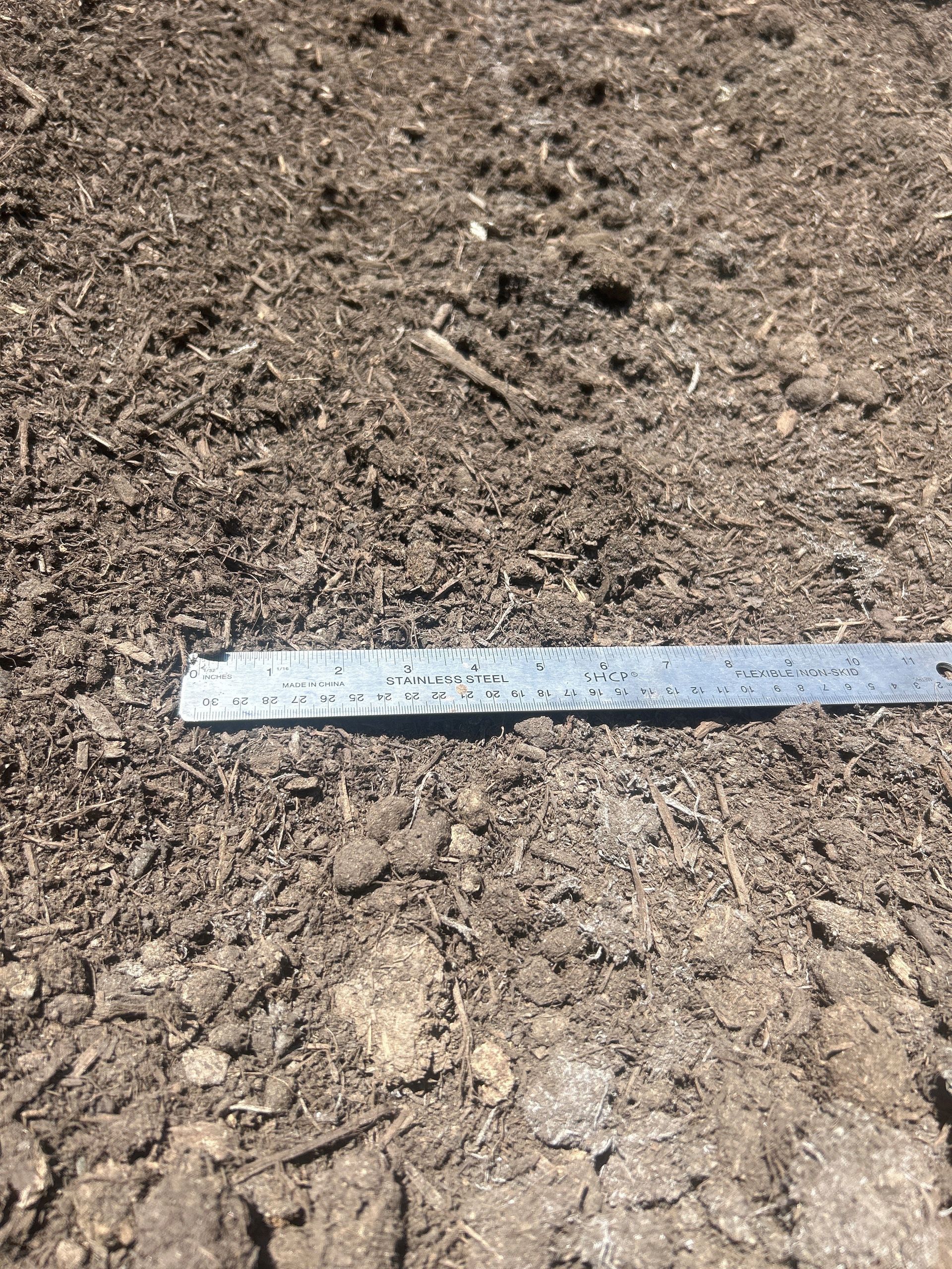 Soil with a metal ruler laid across it, showing dark brown texture.