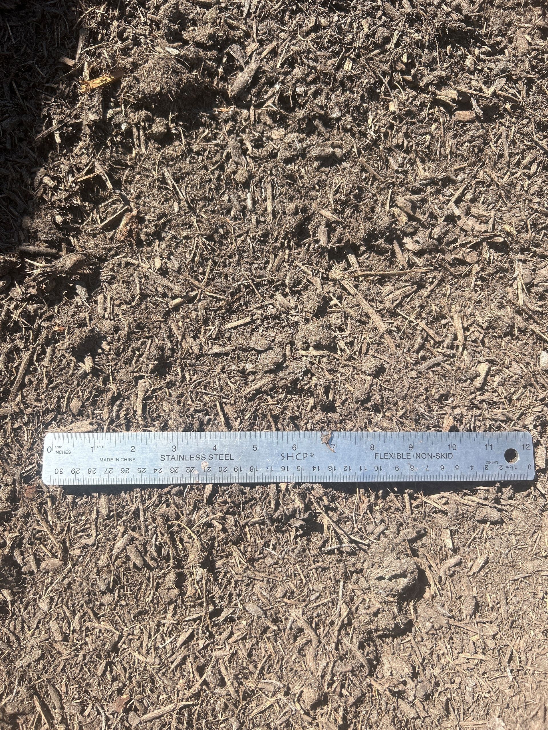 Brown soil and mulch texture with a metal ruler, outdoors.
