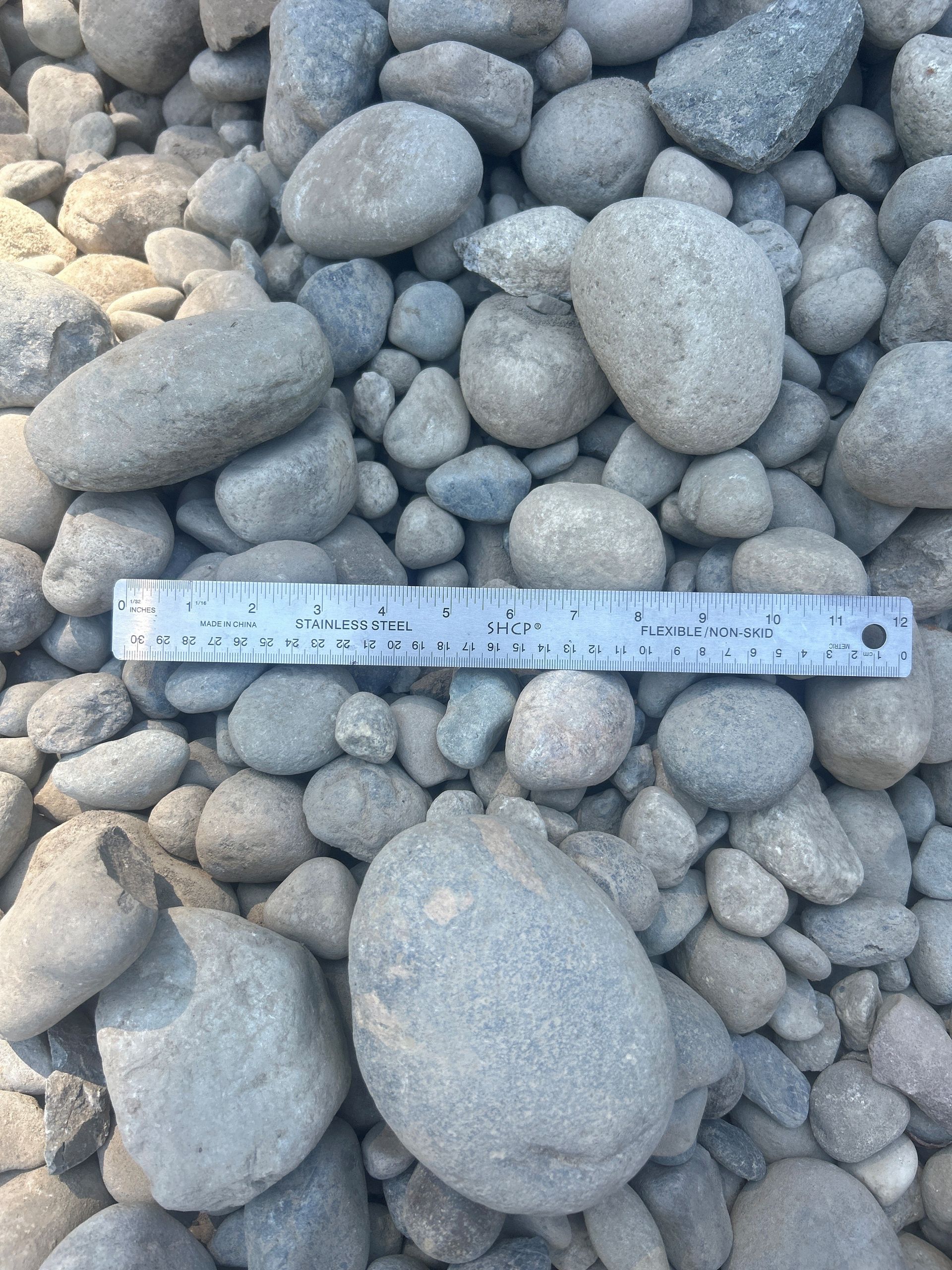Rounded gray river rocks with a metal ruler for scale.