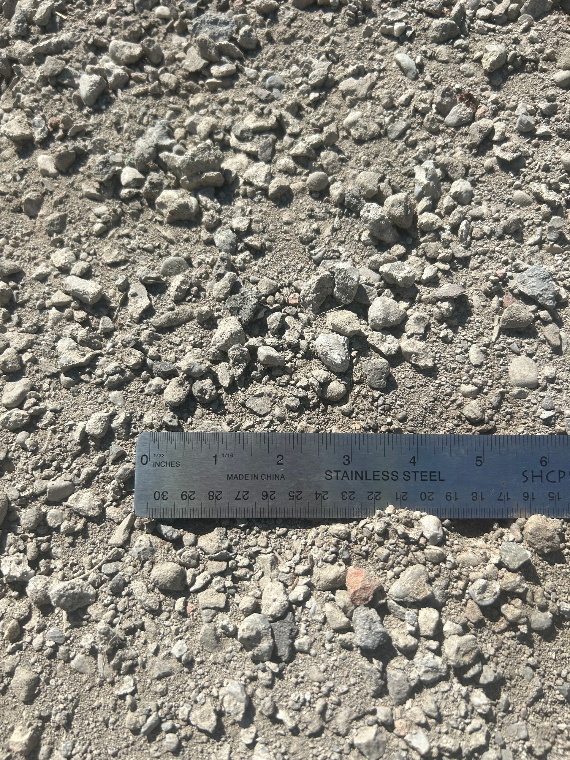 Gravel aggregate with a ruler for scale. Gray and tan stones of varying sizes.