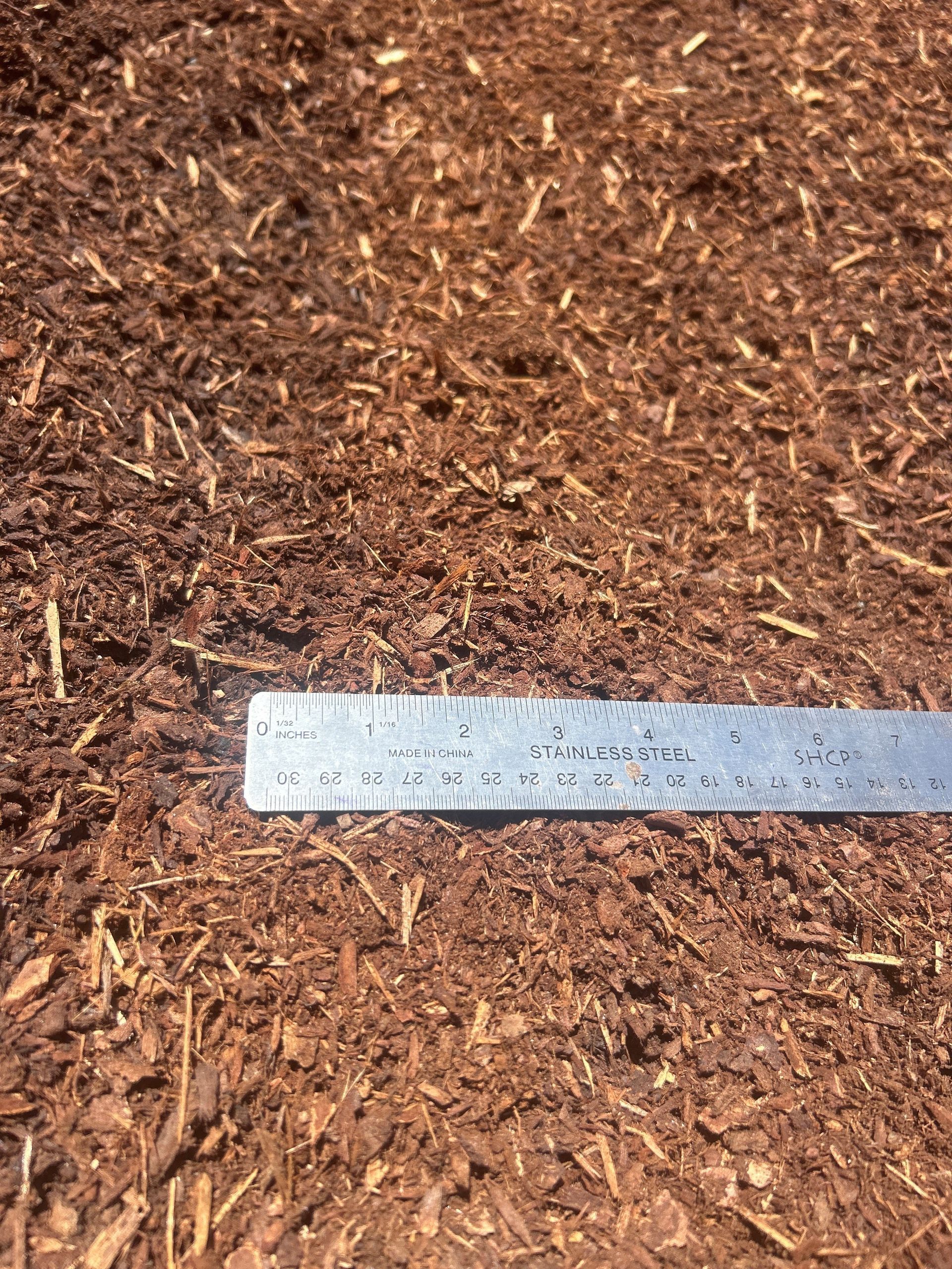 Brown mulch with a metal ruler laid across it.