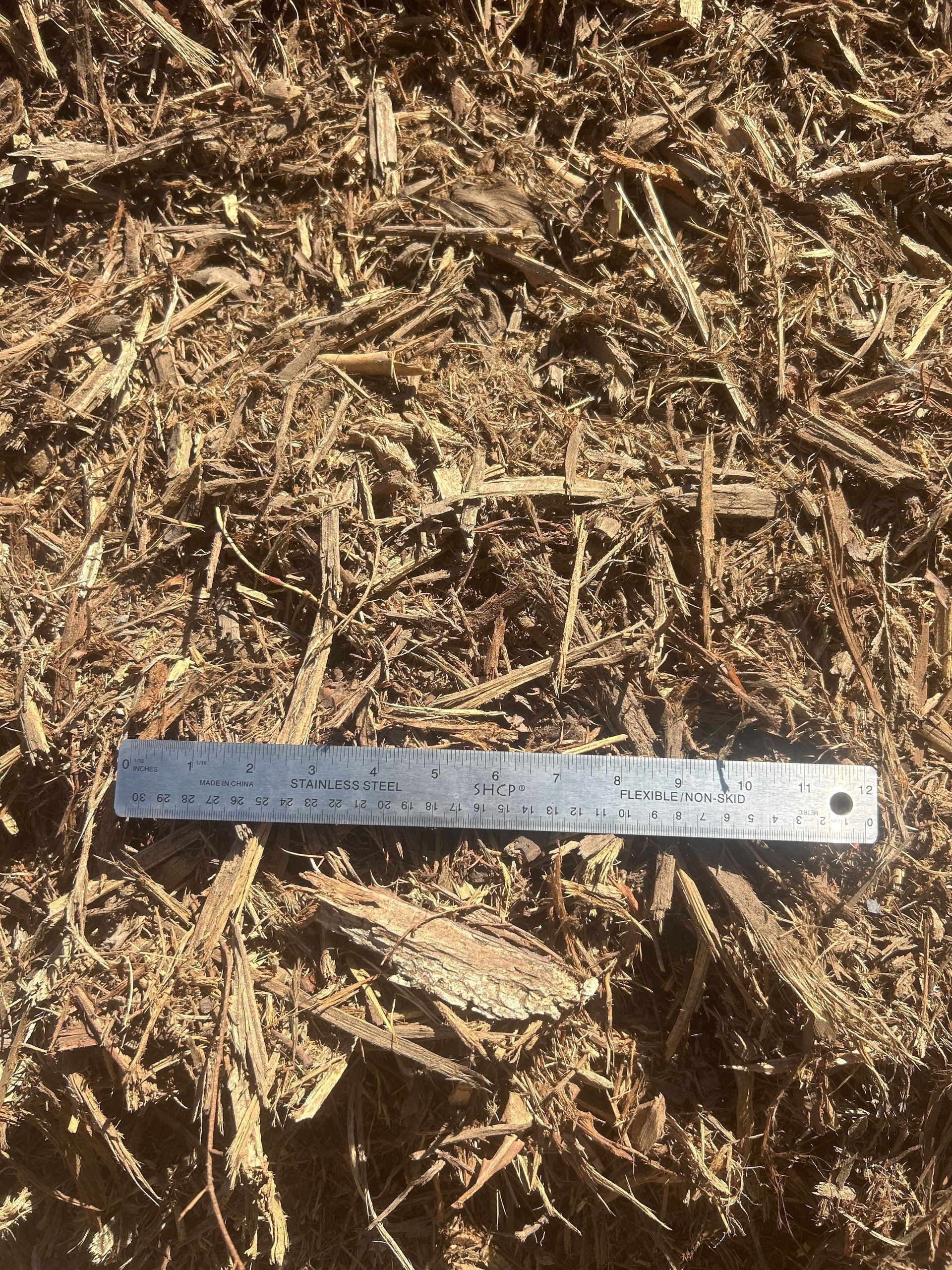 Brown wood mulch with a metal ruler on top.