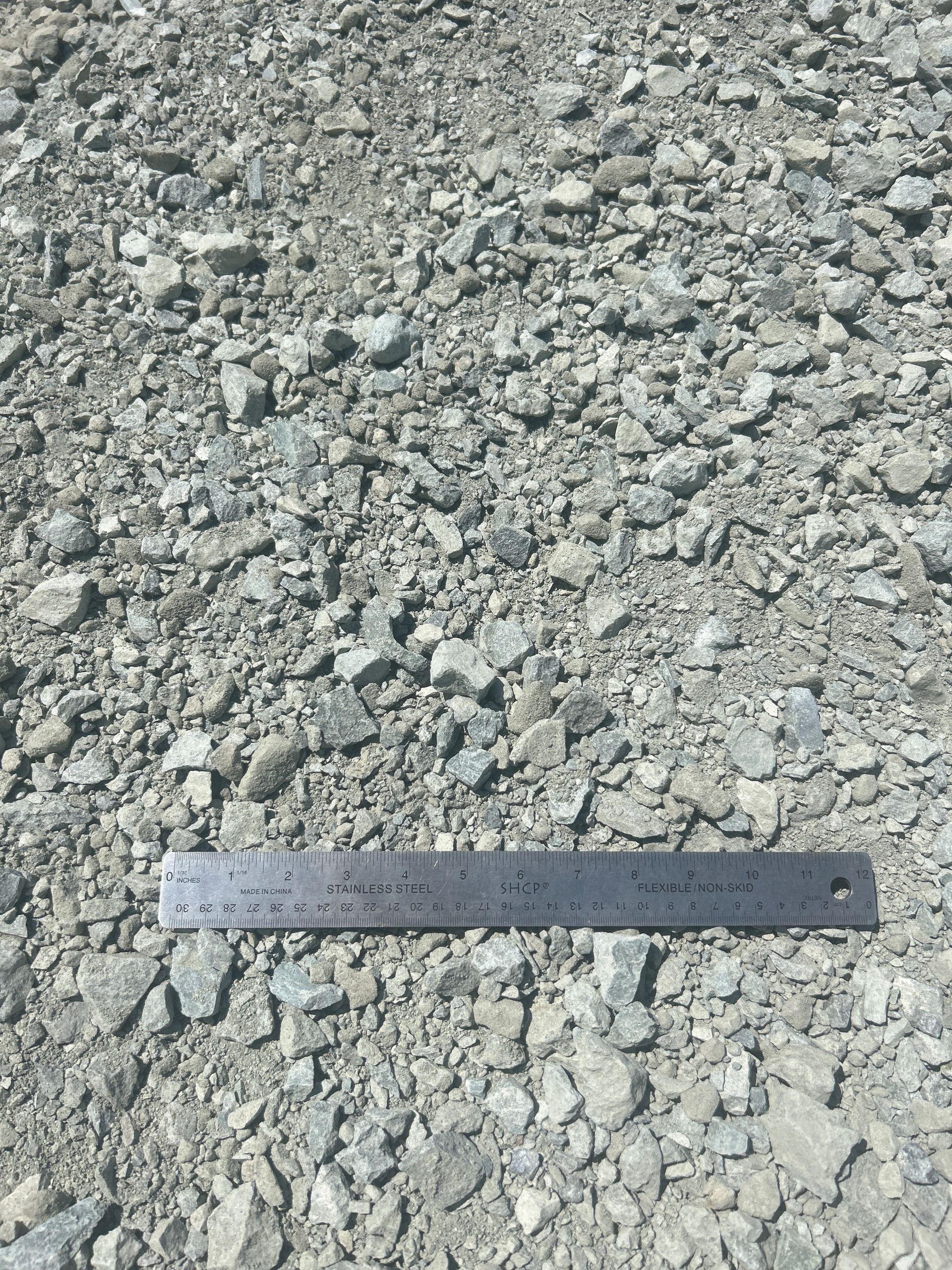 Gravel with various sized gray and light gray stones. A metal ruler rests on top.