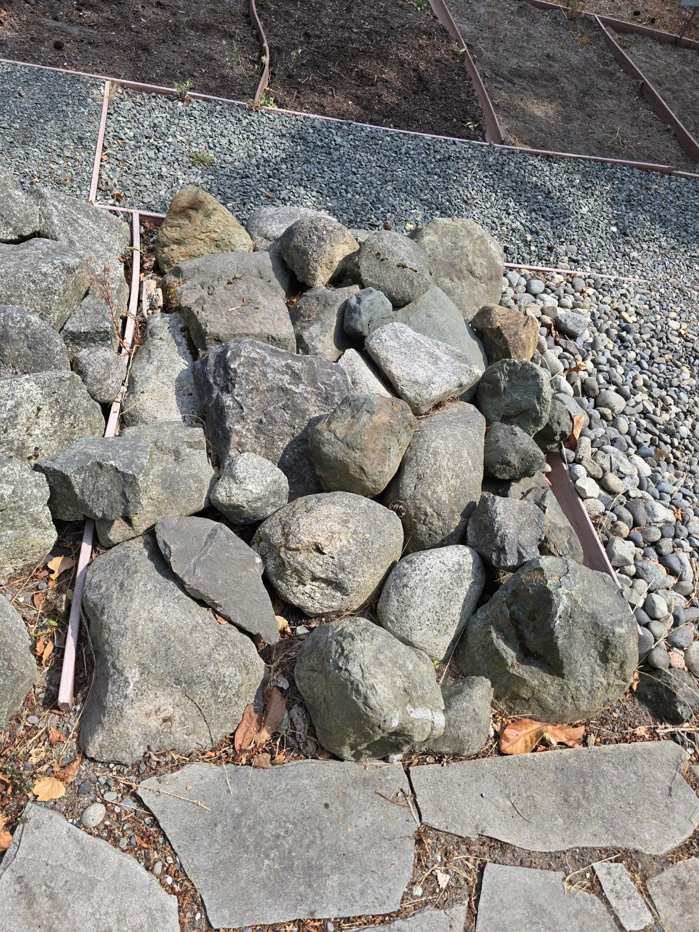 Pile of gray rocks in a stone-bordered area, surrounded by pebbles and a stone path.