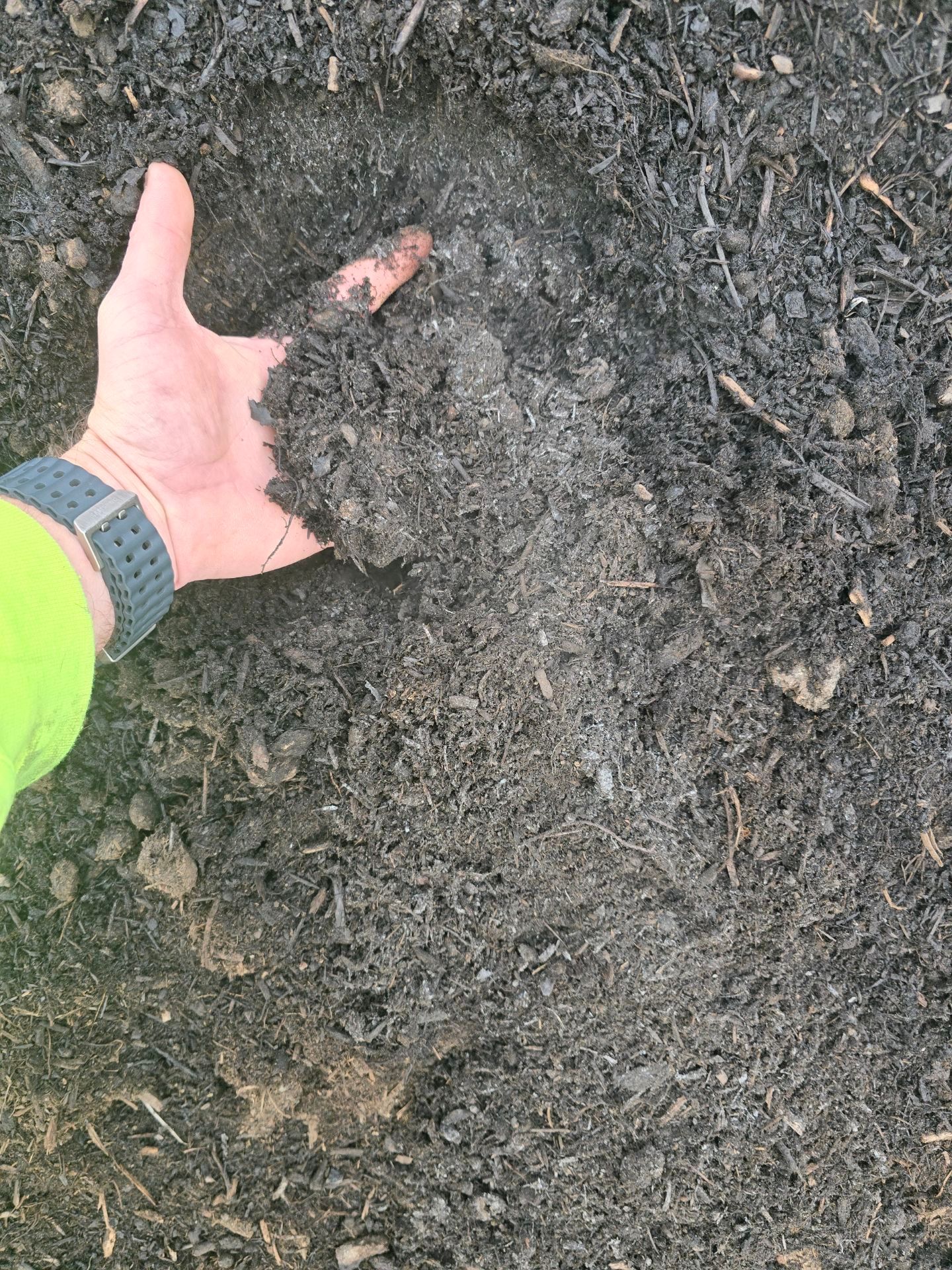 Close-up of dark brown soil with a metal ruler laid across it, possibly in a garden or planting area.