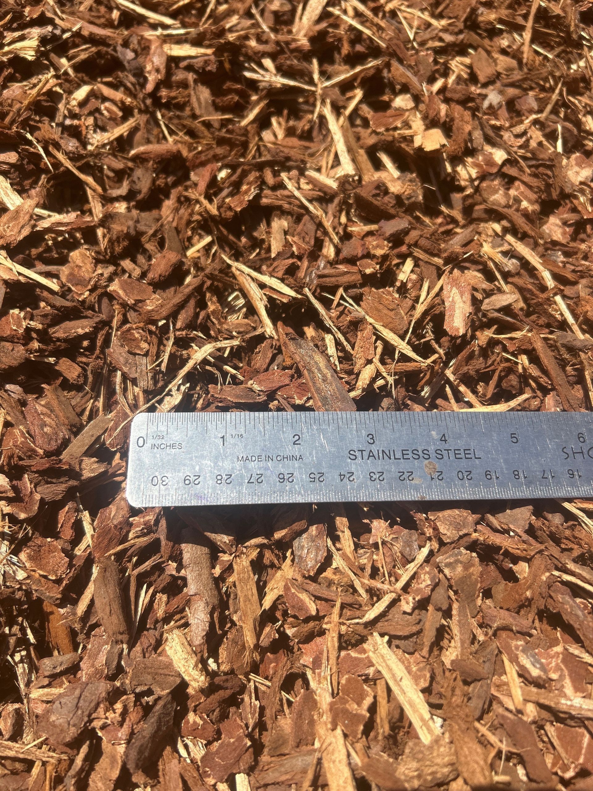Brown shredded bark mulch with a ruler for scale.