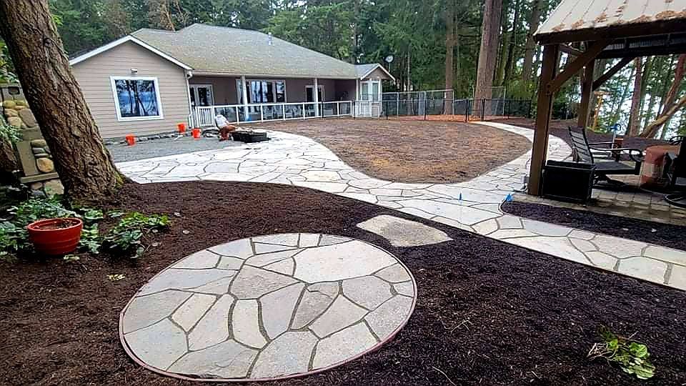 Stone pathways lead through a landscaped yard towards a house and a gazebo with a view.