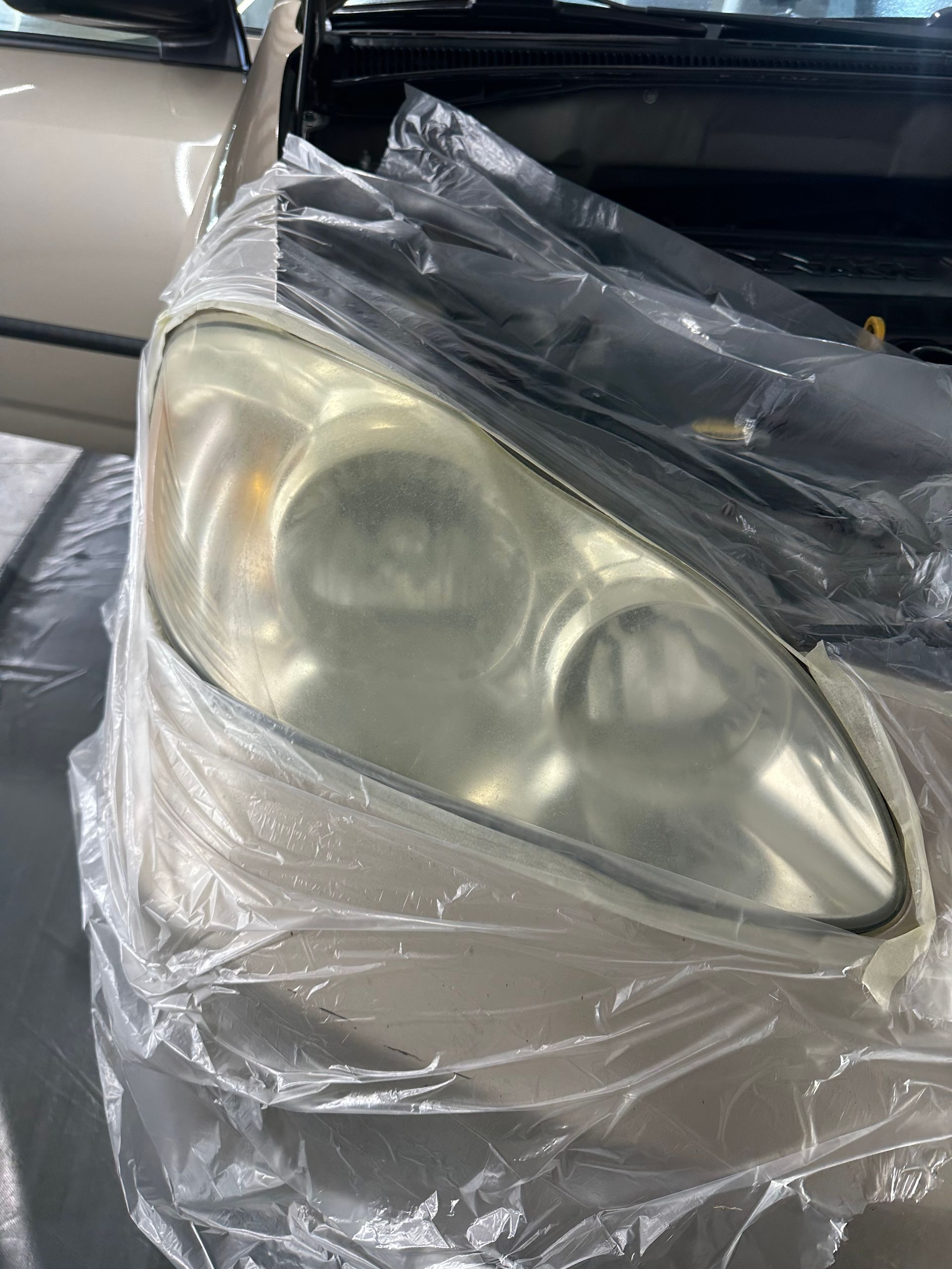 A close up of a car headlight wrapped in plastic.