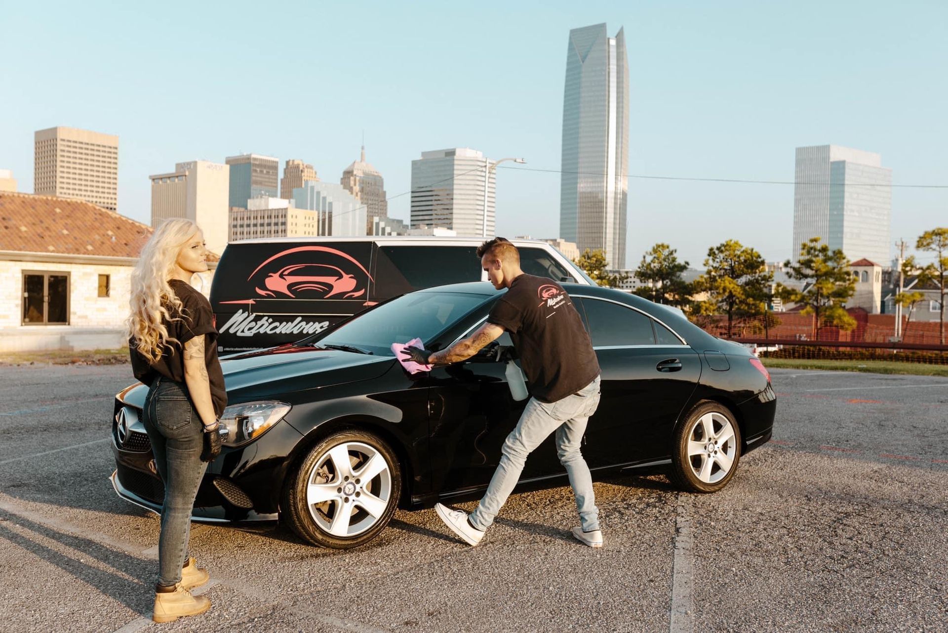 A man and a woman are standing next to a black car in a parking lot.