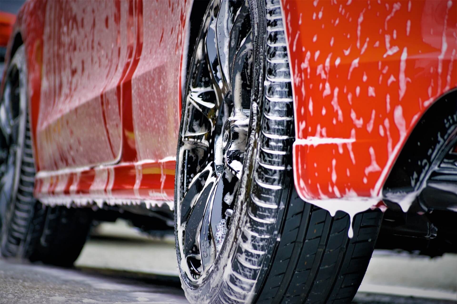 A red car is being washed with soap and water.