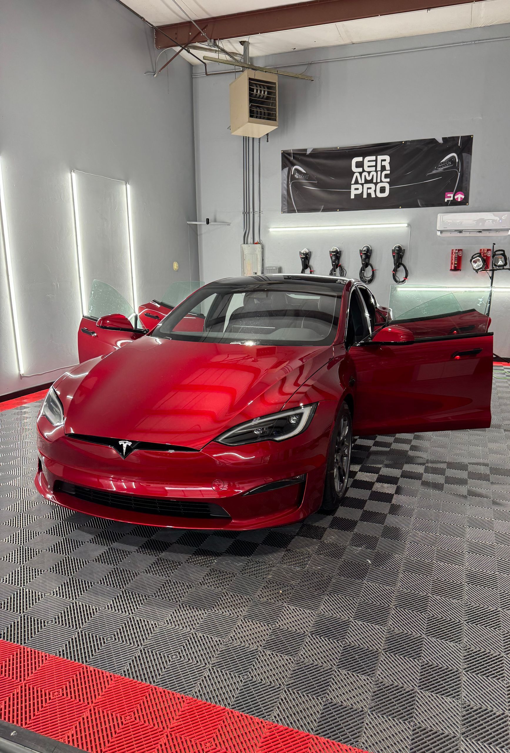 A red tesla model s is parked in a garage with its doors open.