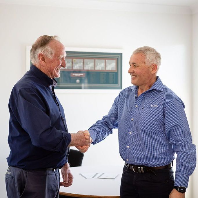 Two men shaking hands in front of a white board