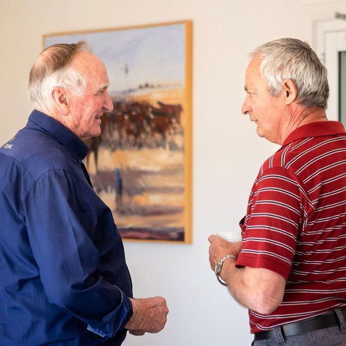 Two men are talking in front of a painting on the wall