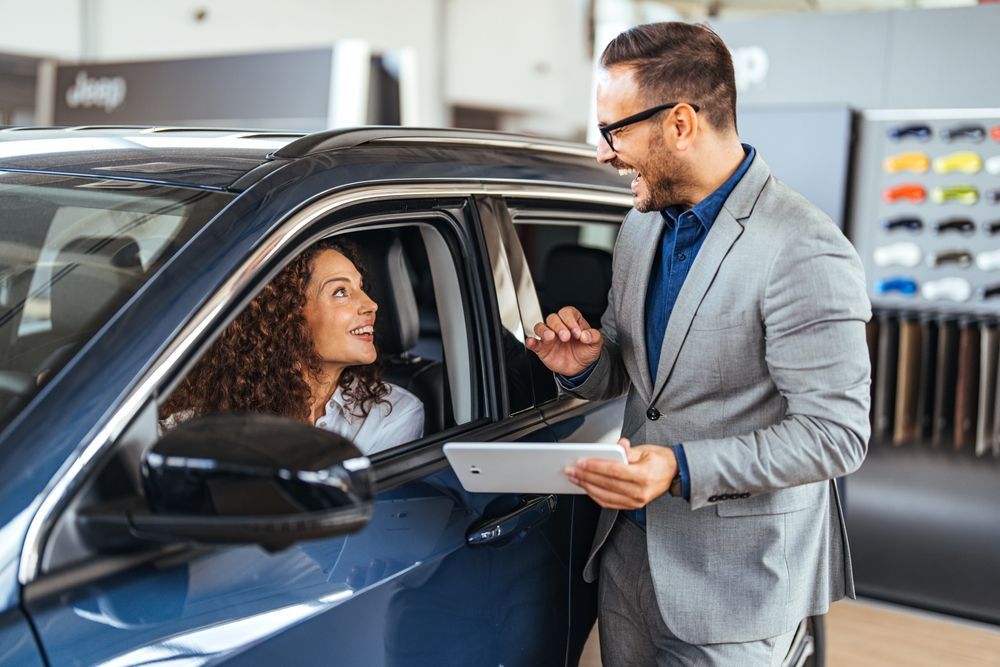 A man is holding a tablet while talking to a woman in a car.