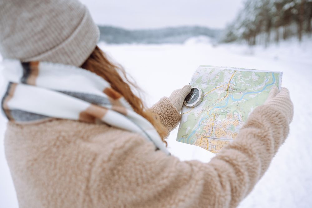 A woman is holding a compass and looking at a map in the snow.