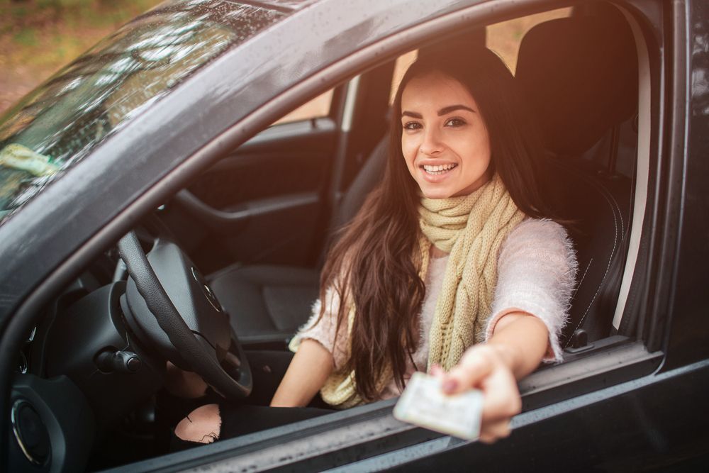 A woman is sitting in a car holding a driving license.