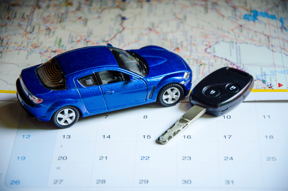 A blue toy car is sitting on top of a calendar next to a car key.