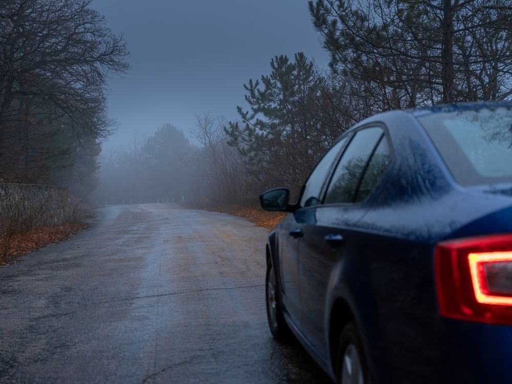 A blue car is parked on the side of a foggy road.