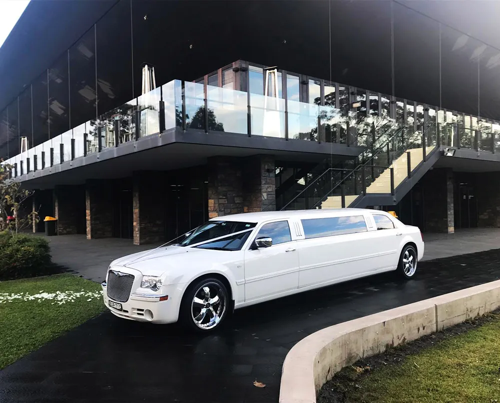 A white limousine is parked in front of a building.