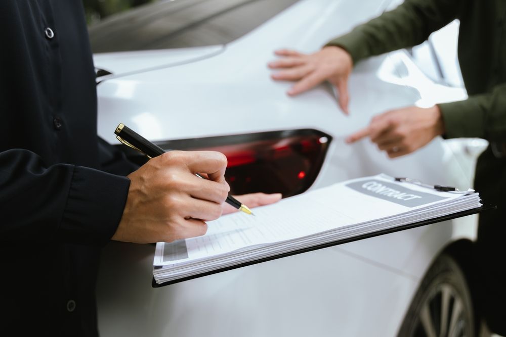 A man is writing on a clipboard in front of a white car.