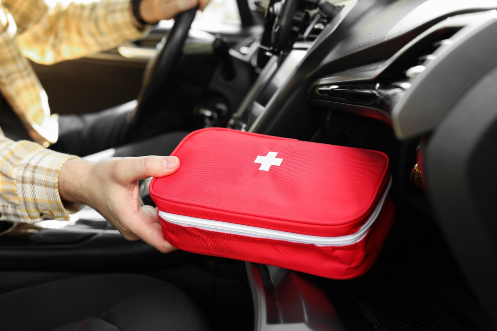 A person is holding a red first aid kit in their car.