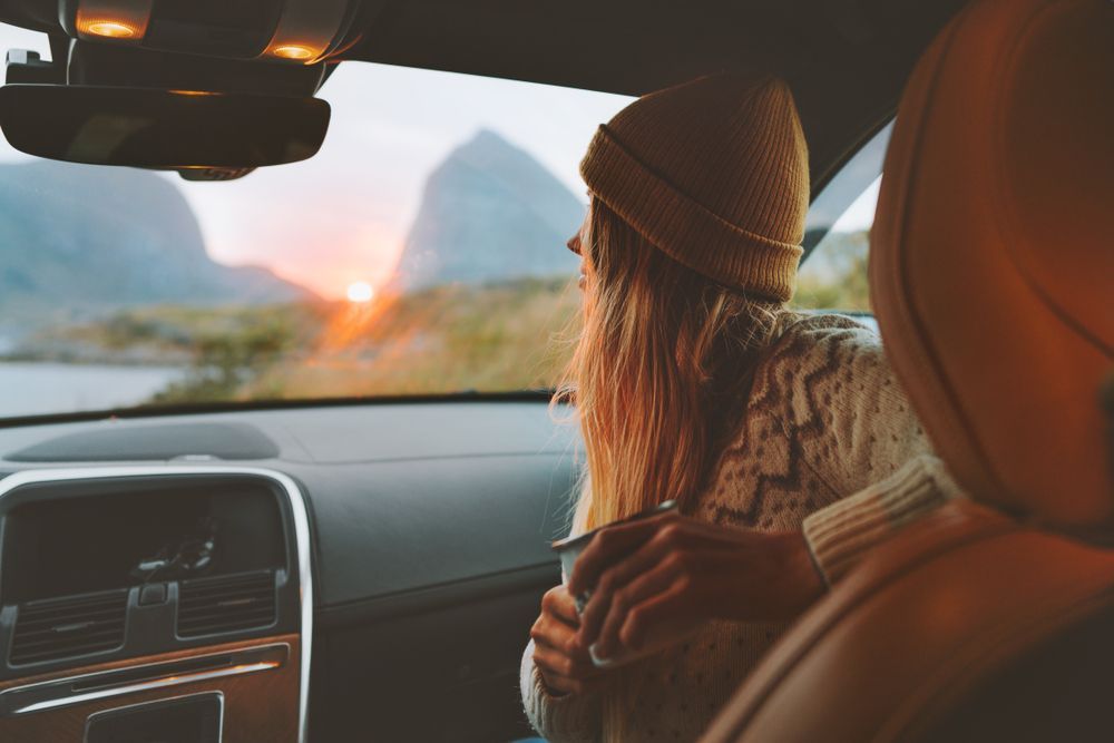 A woman is sitting in the driver 's seat of a car holding a cup of coffee.