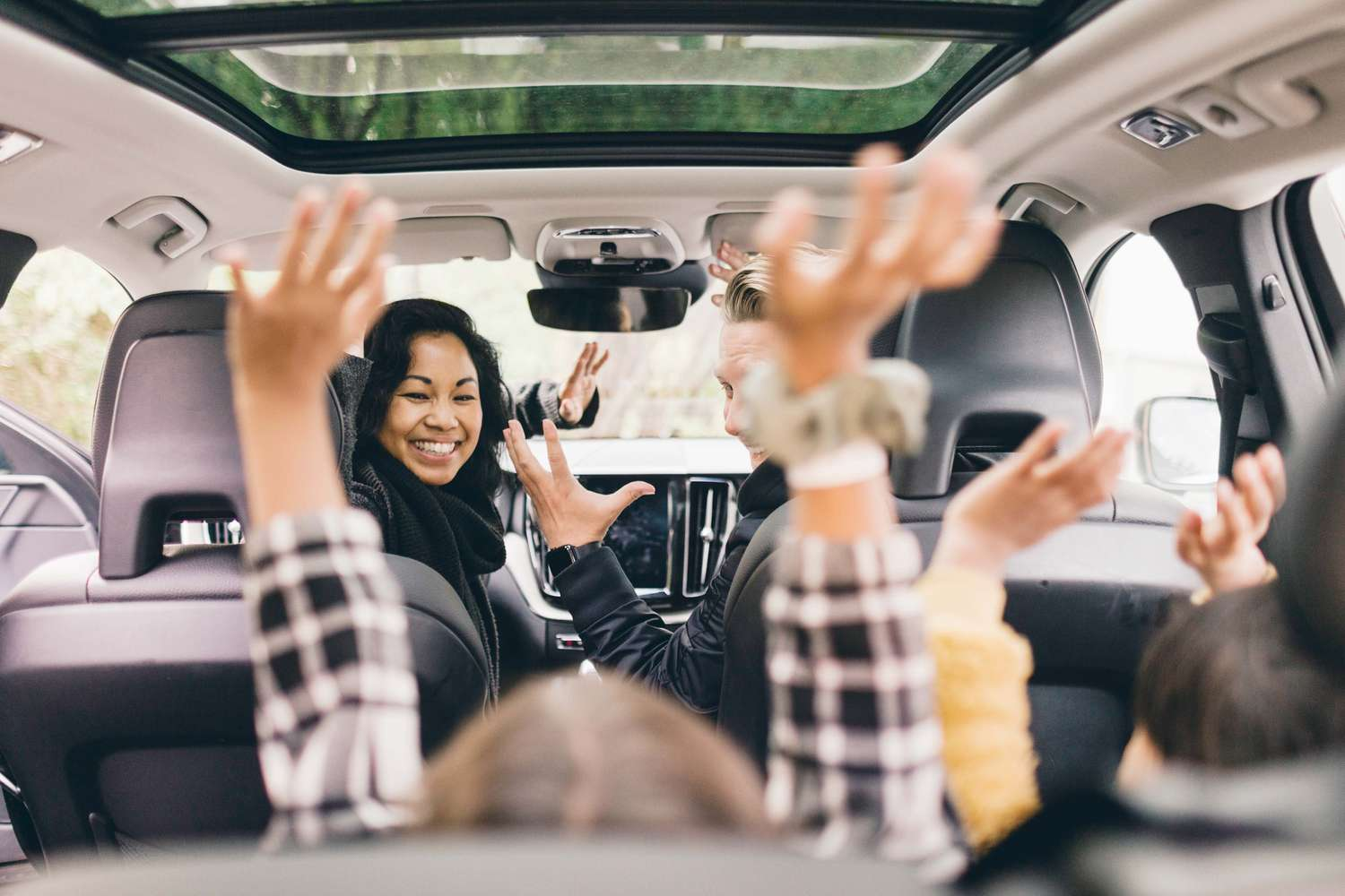 A group of people are sitting in a car with their hands in the air.