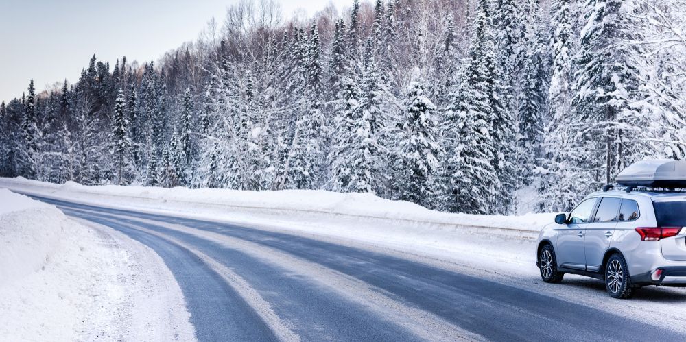 A car with a roof rack is driving down a snowy road.