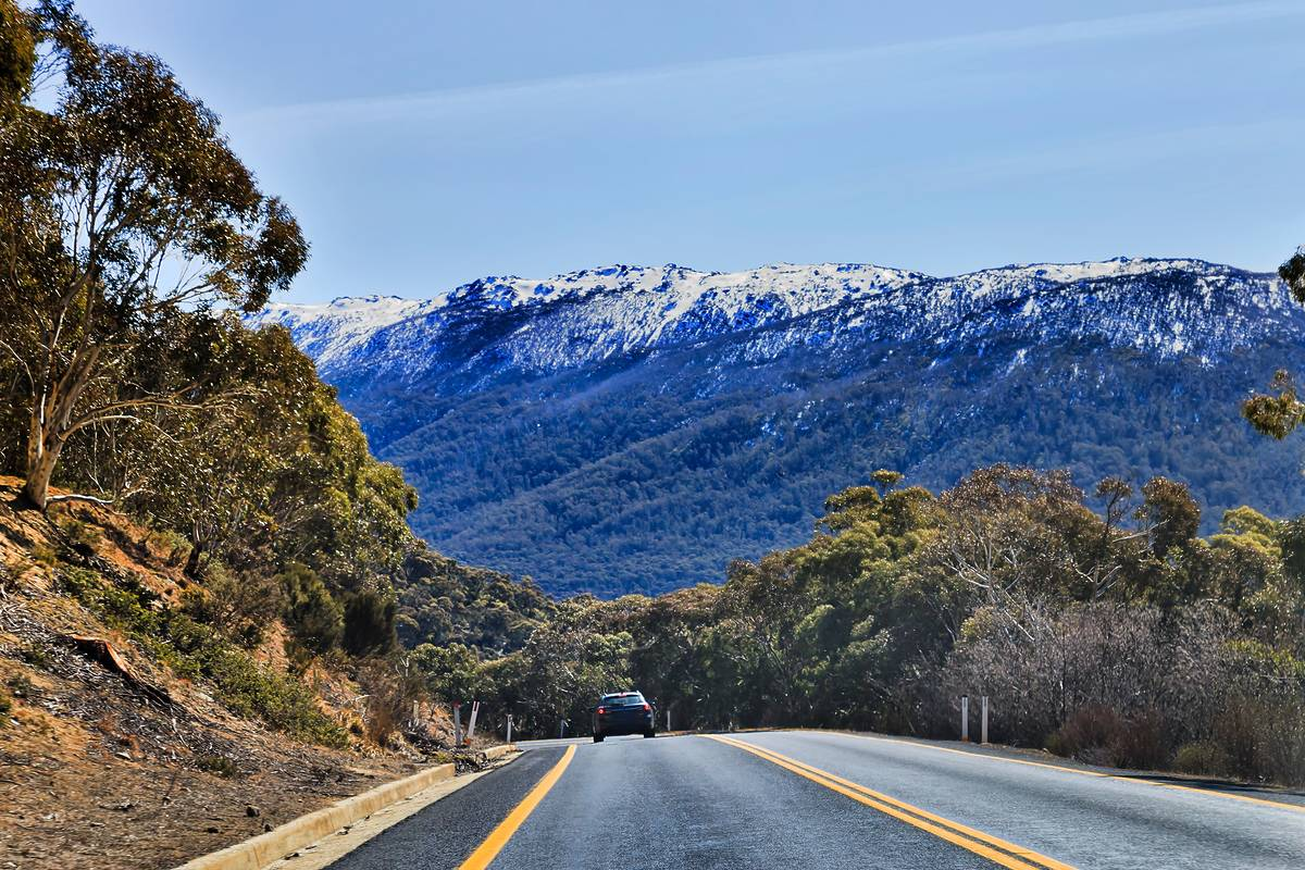 A car is driving down a road with mountains in the background.
